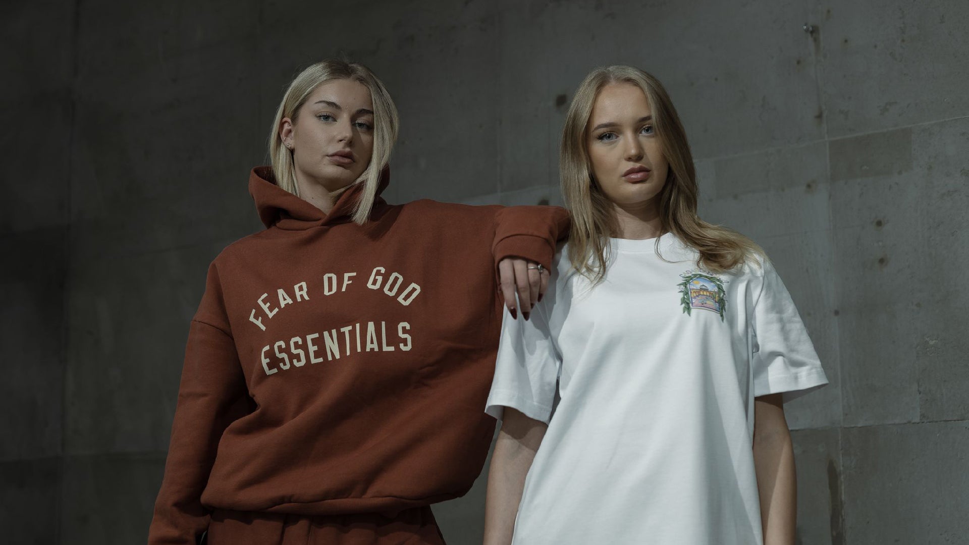 Two people wearing 'Fear of God Essentials' hoodie and a white t-shirt with a graphic design.